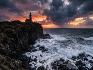 Dramatic ocean cliff at sunset with lighthouse silhouette